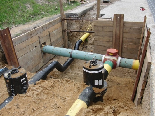 Bestehendes Erdgasnetz (hier ein Hochdrucknetz) mit verschiedenen Komponenten: PE-Leitungen (hier unten rechts), Stahlleitungen (quer durchs Bild laufend), Absperrschieber (hier in schwarz) und Ventile (hier rot)