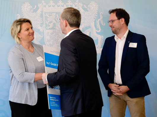 Gloria Geißler-Brems und Patrick Horst von GP Joule die Förderurkunde aus den Händen von Staatsminister Hubert Aiwanger (Mitte) entgegen. 