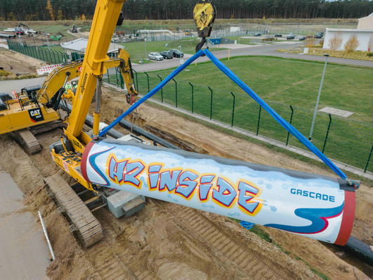 Ein Kran hebt ein großes Pipeline-Segment mit dem Graffiti "Air Inside" auf einer Baustelle an. - © GASCADE